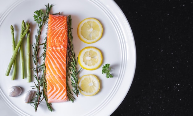 Foto rauwe verse zalmfilet met kruiden en ingrediënten, op witte schotel en zwarte tafel