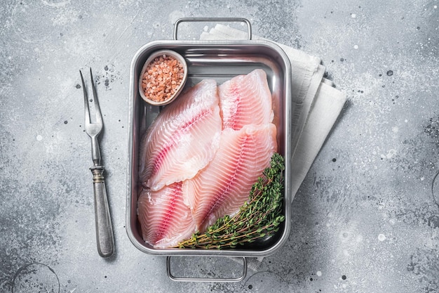 Rauwe witte vis tilapia ongekookte filet in keukenblad met kruiden Grijze achtergrond Bovenaanzicht