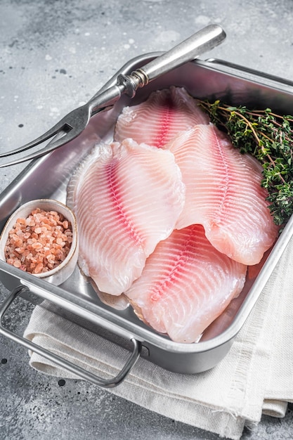 Rauwe witte vis tilapia ongekookte filet in keukenblad met kruiden Grijze achtergrond Bovenaanzicht