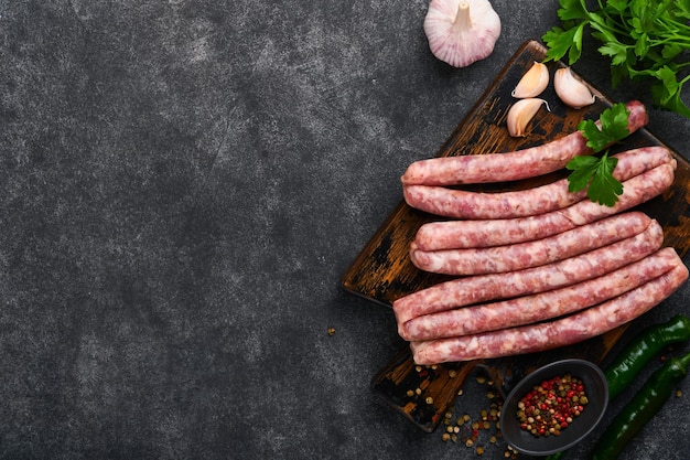 Rauwe worstjes braadworst of worstjes met ingrediënten op snijplank met kruiden op een stenen achtergrond met kopieerruimte voedsel koken achtergrond bovenaanzicht