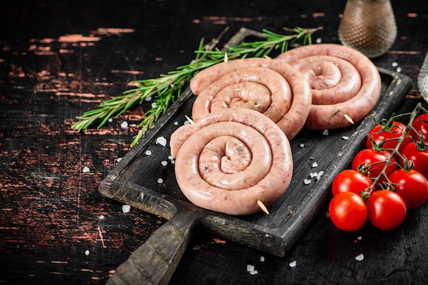 Rauwe worstjes op een snijplank met een takje rozemarijn en tomaten