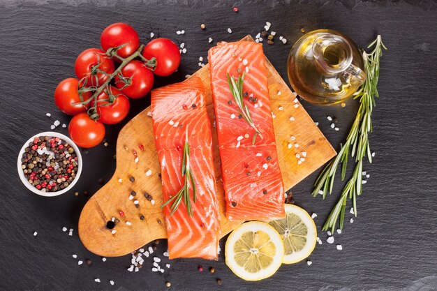 Rauwe zalmfilet en ingrediënten voor het koken op een snijplank en een donkere leiachtergrond. Bovenaanzicht