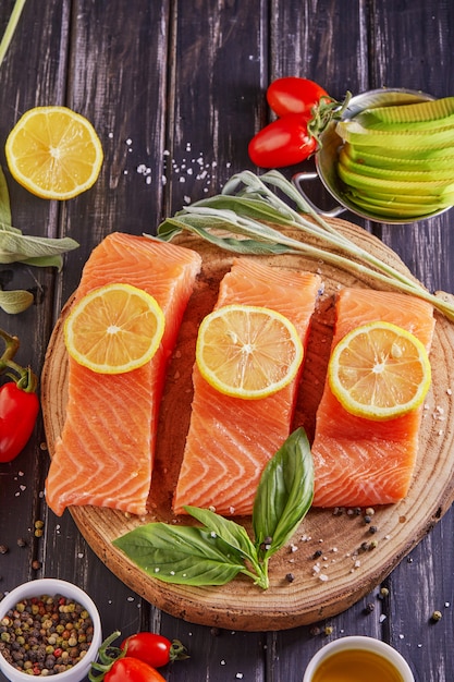 Rauwe zalmfilet in stukjes gesneden, peper zout dille citroen rozemarijn en cherry tomaten op een donkere houten tafel.