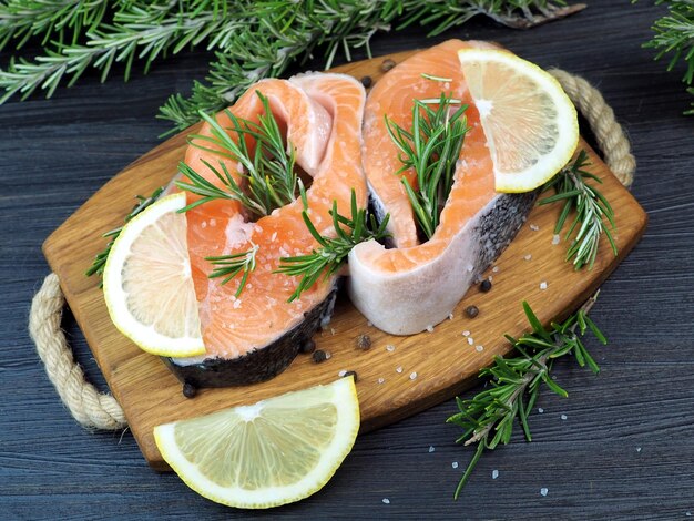 Rauwe zalmsteaks met schijfjes citroen rozemarijn takjes grof zeezout op een houten bord