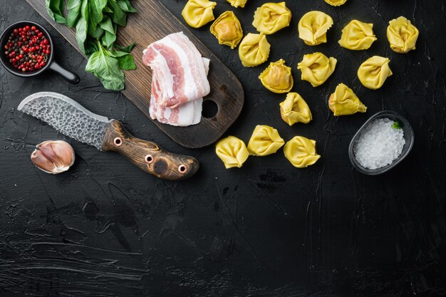 Rauwe zelfgemaakte Tortellini met gezouten ham set, op zwarte achtergrond, bovenaanzicht plat lag, met kopieerruimte voor tekst