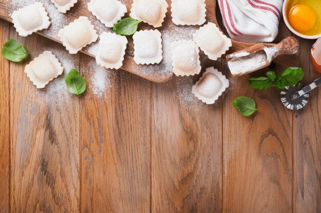 Ravioli cibo italiano gustosi ravioli di pasta fatta in casa con farina pomodori uova e verdure basilico su fondo in legno processo di produzione dei ravioli italiani sfondo degli ingredienti per la cottura degli alimenti vista dall'alto