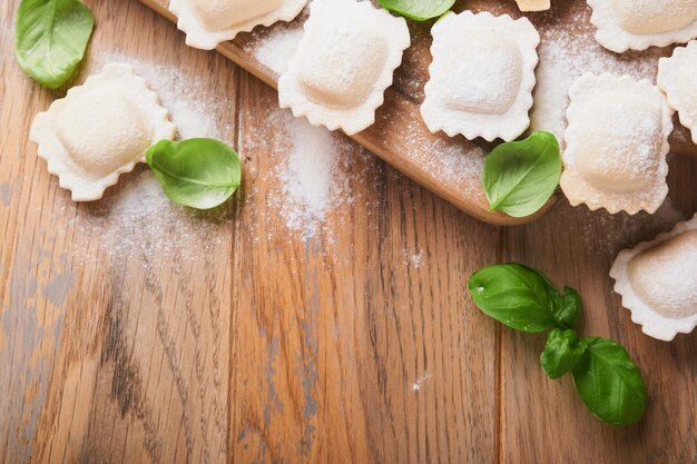 Ravioli cibo italiano gustosi ravioli di pasta fatta in casa con farina pomodori uova e verdure basilico su fondo in legno processo di produzione dei ravioli italiani sfondo degli ingredienti per la cottura degli alimenti vista dall'alto