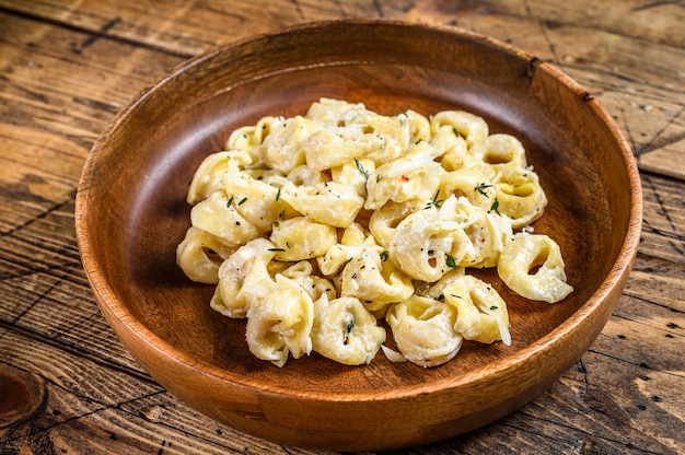 Ravioli of tortellini pasta in roomkaas saus met vlees op houten tafel. Bovenaanzicht.