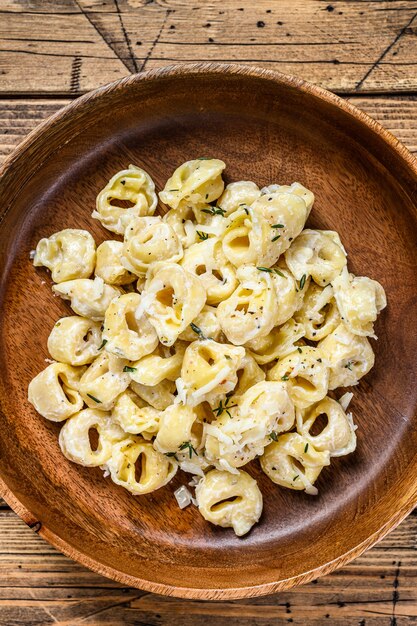 Ravioli of tortellini pasta in roomkaassaus met vlees. houten achtergrond. Bovenaanzicht.