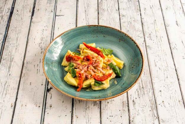 Ravioli stuffed with meat with pieces of smoked bacon basil leaves and dehydrated tomatoes in a blue bowl