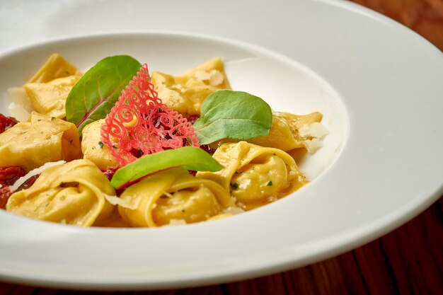 Foto ravioli con diversi ripieni in salsa e parmigiano in un piatto bianco su fondo di legno