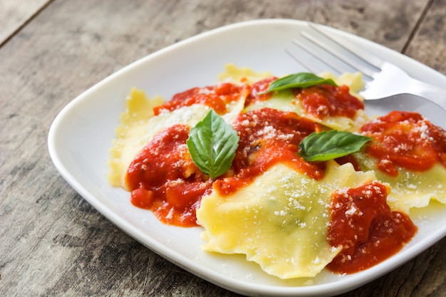 Ravioli with tomato sauce and basil on wooden background.