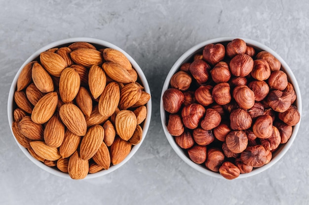 Raw almonds and hazelnuts in bowl on gray background Top view