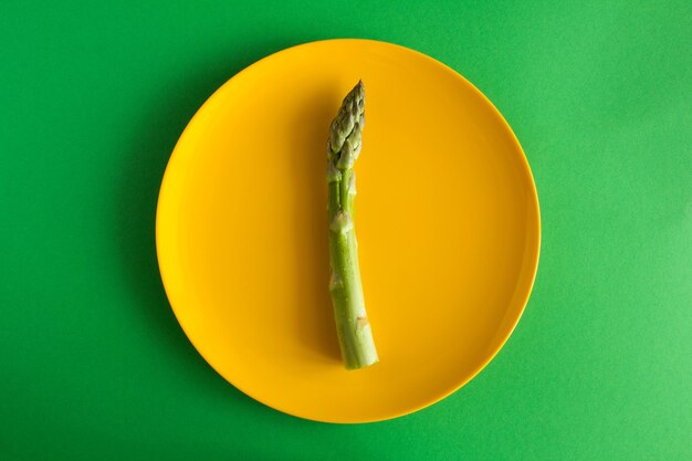 Raw  asparagus  in the yellow  plate  on the green  background.Top view.Diet minimal concept.