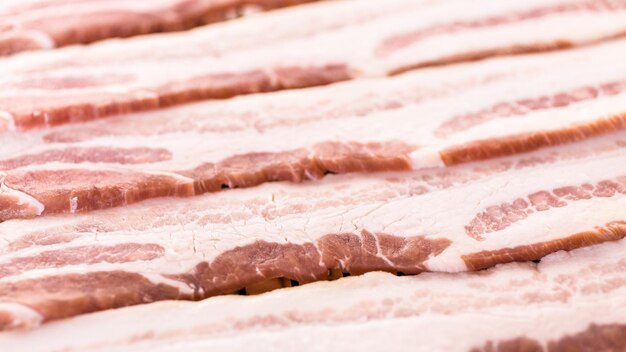 Raw bacon strips on a baking sheet.