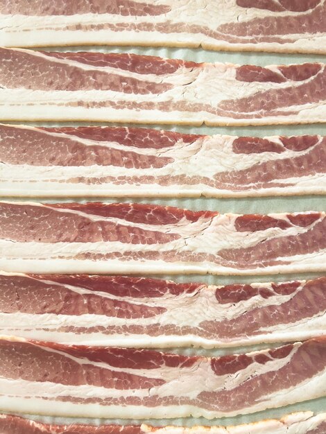 Photo raw bacon strips ready for cooking on a baking tray