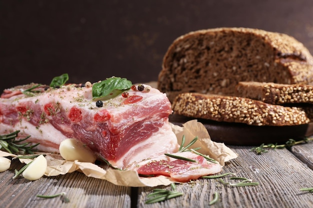 Raw bacon with bread and spices on wooden table