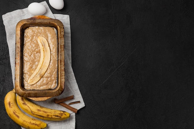 Сырое тесто для бананового хлеба в прямоугольной форме для выпечки с ингредиентами на черном фоне