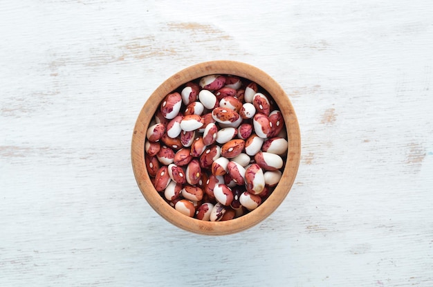 Raw beans in a bowl on a white wooden background.