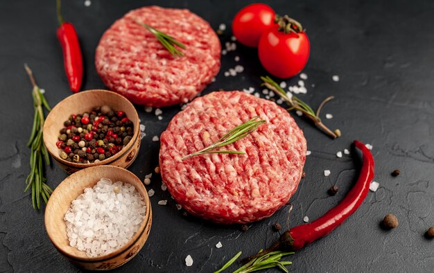 Raw beef burger cutlets with herbs and spices on a concrete background