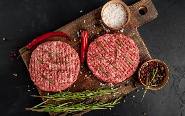 Raw beef burger cutlets with herbs and spices on a concrete background