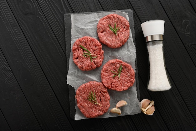 Raw beef burger patties on butcher's wooden board rosemary and pepper Black background View from above