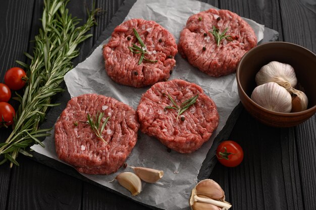 Raw beef burger patties on butcher's wooden board rosemary and pepper Black background View from above