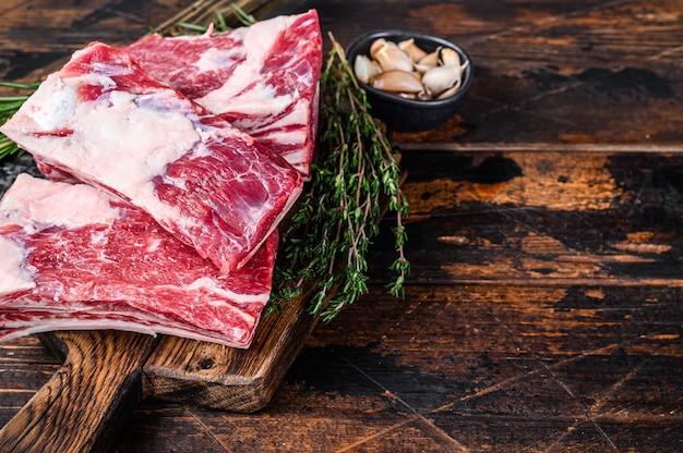 Raw beef calf short ribs meat on a butcher cutting board with cleaver. Dark wooden background. Top view. Copy space.