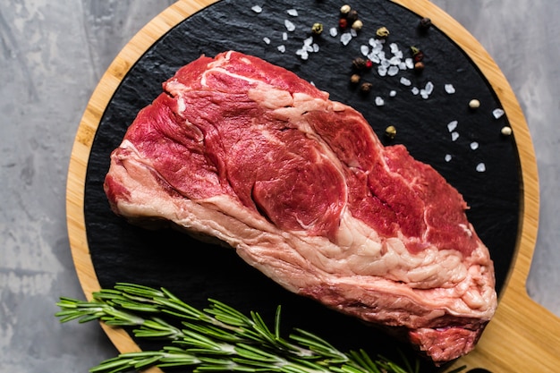 Raw beef on a cutting board with rosemary and spices