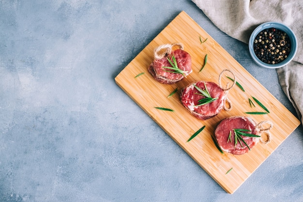 Raw beef filet mignon steak on a wooden board with rosemary and spices