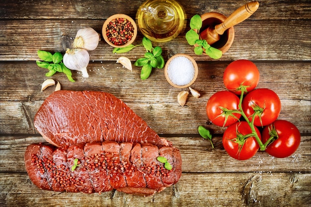 Carne di filetto di manzo crudo con pomodori, erbe e spezie sulla tavola di legno.