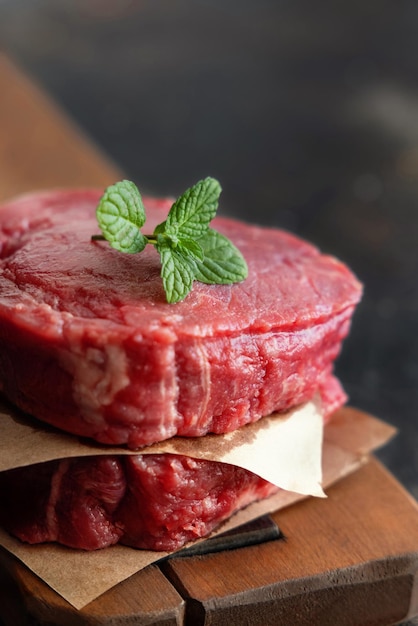 Raw beef fillet steaks on wooden board on dark background close up Portioned filet mignons with spices and ingredients Concept of summer food