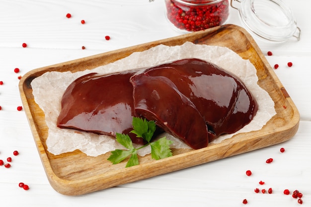 Raw beef liver on wooden board on table