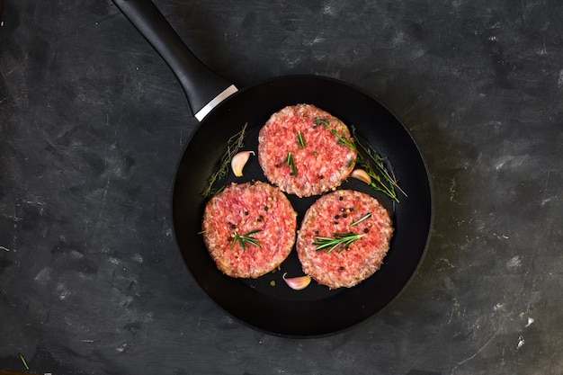 Котлеты стейка бургера сырого мяса говядины в сковороде на черном столе.