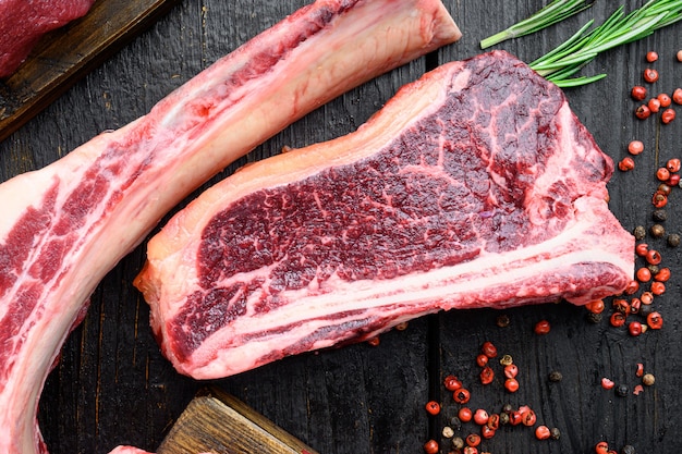 검은 나무 테이블에 있는 뼈 스테이크 세트에 있는 생 쇠고기 고기 클럽 또는 스트립로인