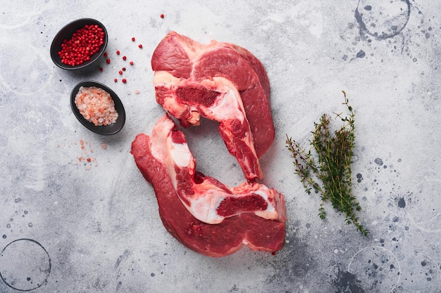 Raw beef meat Rough piece of meat on bone for roast or soup with salt pepper thyme and rosemary on old grey concrete table background Entrecote Raw cowboy steak Top view