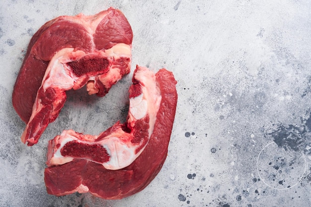 Raw beef meat Rough piece of meat on bone for roast or soup with salt pepper thyme and rosemary on old grey concrete table background Entrecote Raw cowboy steak Top view