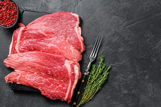 Raw beef meat round steak on a marble board.  Black background. Top view. Copy space.