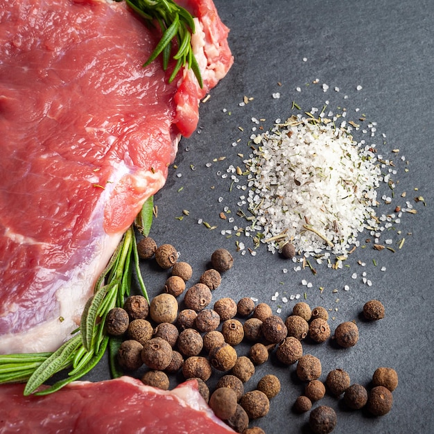 Raw beef meat and salt Two slices of fresh raw meat rosemary and fresh herbs on a black stone plate