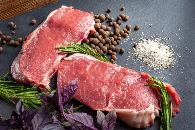 Raw beef meat Two slices of fresh raw meat rosemary and fresh herbs on a black slate stone plate