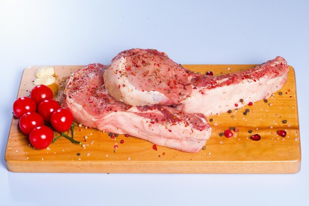 Raw beef meat and vegetables on a wooden board, on a neutral background.