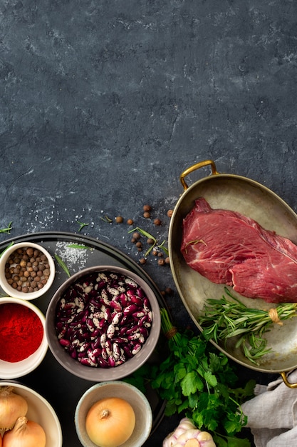 健康的な食品を調理するための原料と生の牛肉。調理済みの牛肉とハーブ、スパイス、豆のトップビュー