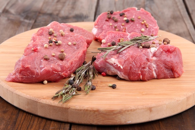 Raw beef meat with spices on cutting board on wooden background