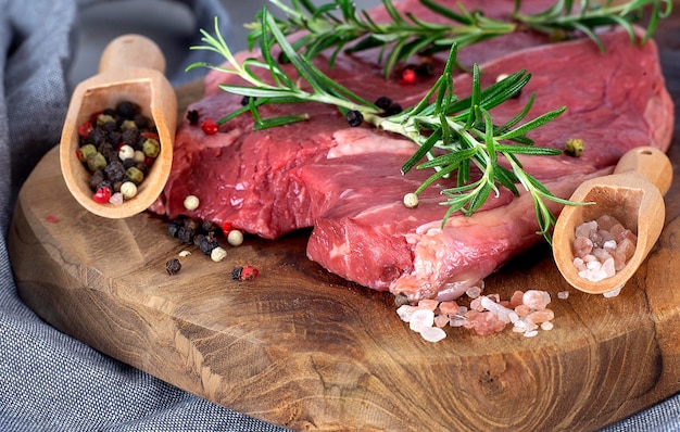 Raw beef meat on a wooden cutting board with pepper and salt on wooden spoon