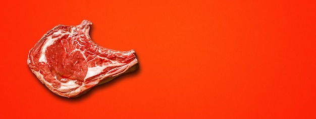 Raw beef prime rib isolated on red background. Top view. Horizontal banner