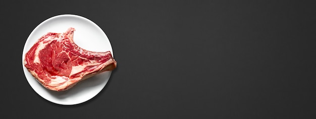 Raw beef prime rib and plate isolated on black background. Top view. Horizontal banner