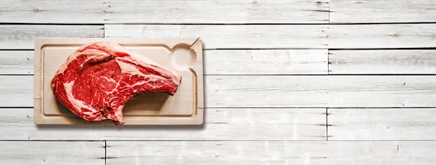 Raw beef prime rib and wooden cutting board isolated on white wooden background. Top view. Horizontal banner