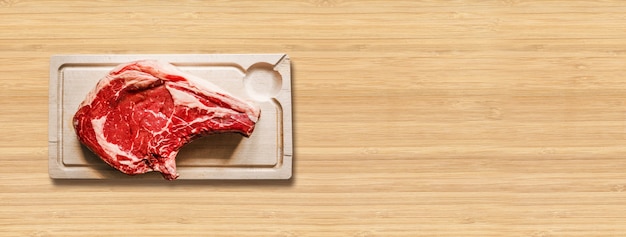 Raw beef prime rib and wooden cutting board isolated on wooden background. Top view. Horizontal banner