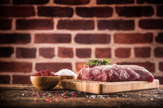 Raw beef ribe-eye steak with salt pepper and herbs on wooden butcher board.