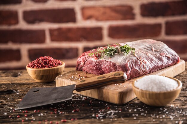 Raw beef ribe-eye steak with salt pepper and herbs on wooden butcher board.